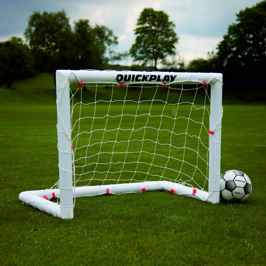 Miniportería de fútbol Q-FOLD 90 x 75 cm con marco y red blancos sobre hierba, con un balón al lado.