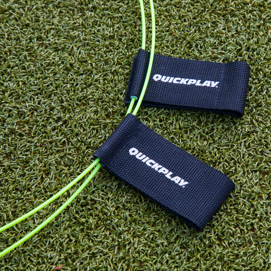 Primer plano de las dianas para portería KICKSTER sobre césped artificial, con dos correas negras QUICKPLAY en los aros amarillos.