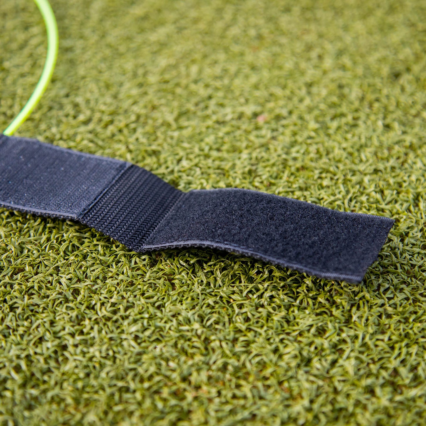 Correa de una diana para portería KICKSTER abierta sobre césped artificial, mostrando el cierre de velcro negro.