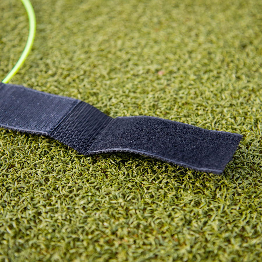 Correa de una diana para portería KICKSTER abierta sobre césped artificial, mostrando el cierre de velcro negro.