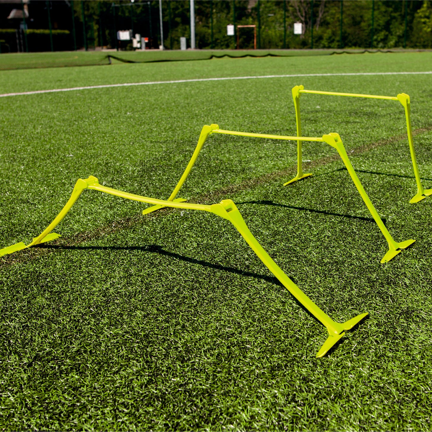 Vallas de entrenamiento regulables amarillas, colocadas a distintas alturas en un campo de césped artificial al sol.