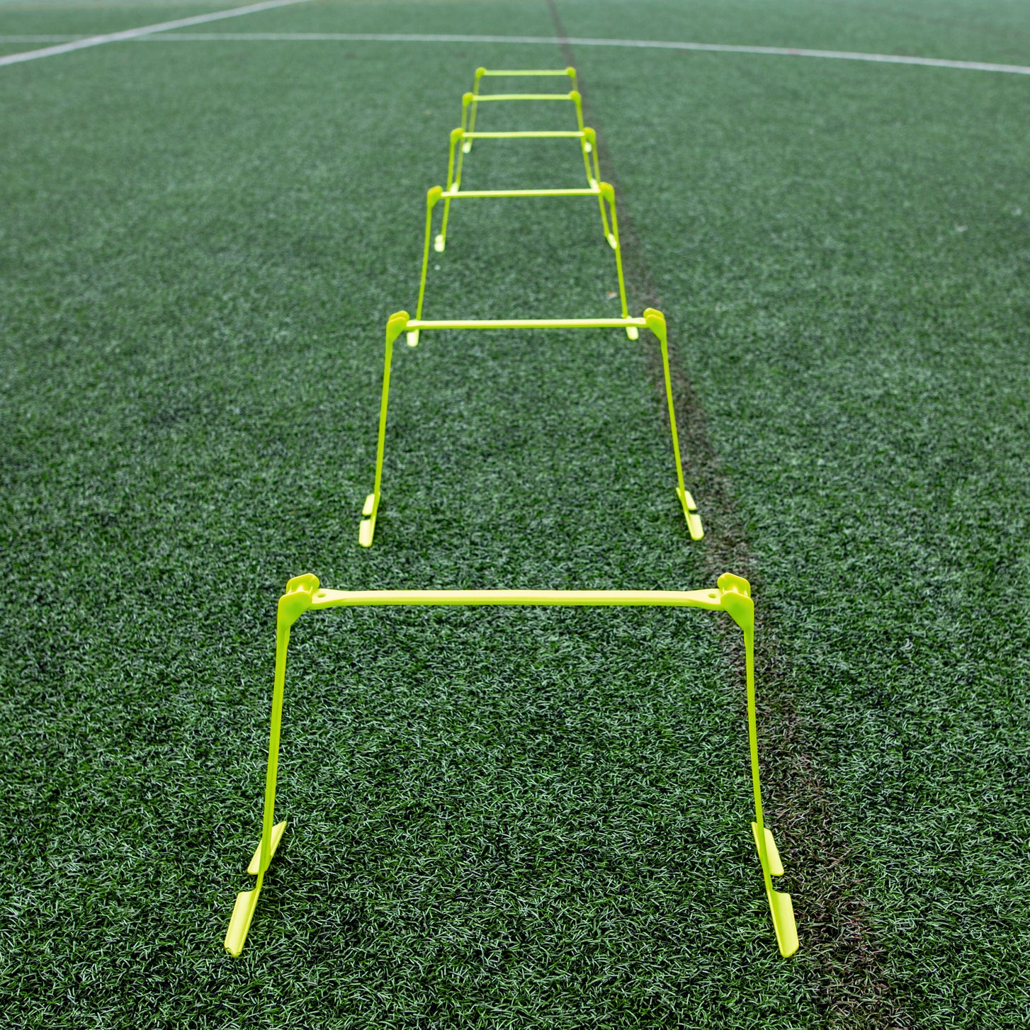 Vallas de entrenamiento regulables colocadas en línea recta en un campo de césped artificial, vistas desde un extremo.
