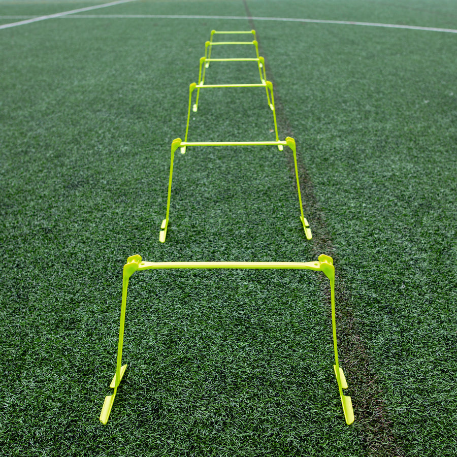 Vallas de entrenamiento regulables colocadas en línea recta en un campo de césped artificial, vistas desde un extremo.