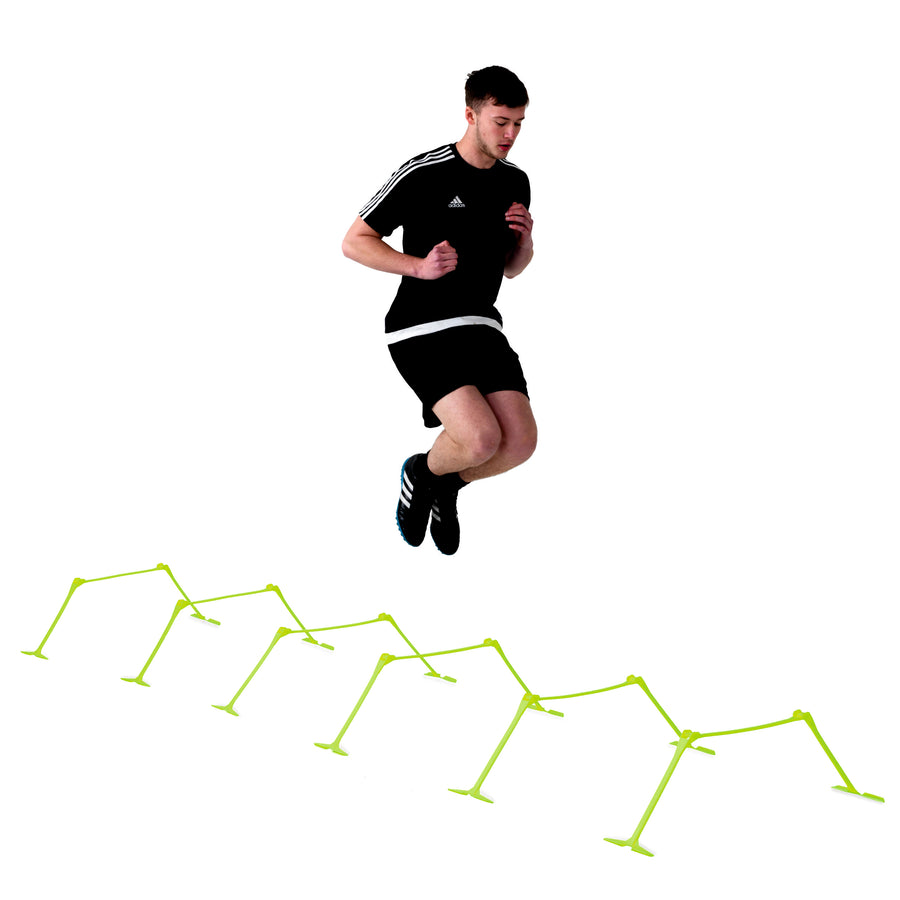 Jugador saltando una fila de vallas de entrenamiento regulables amarillas, sobre fondo blanco.