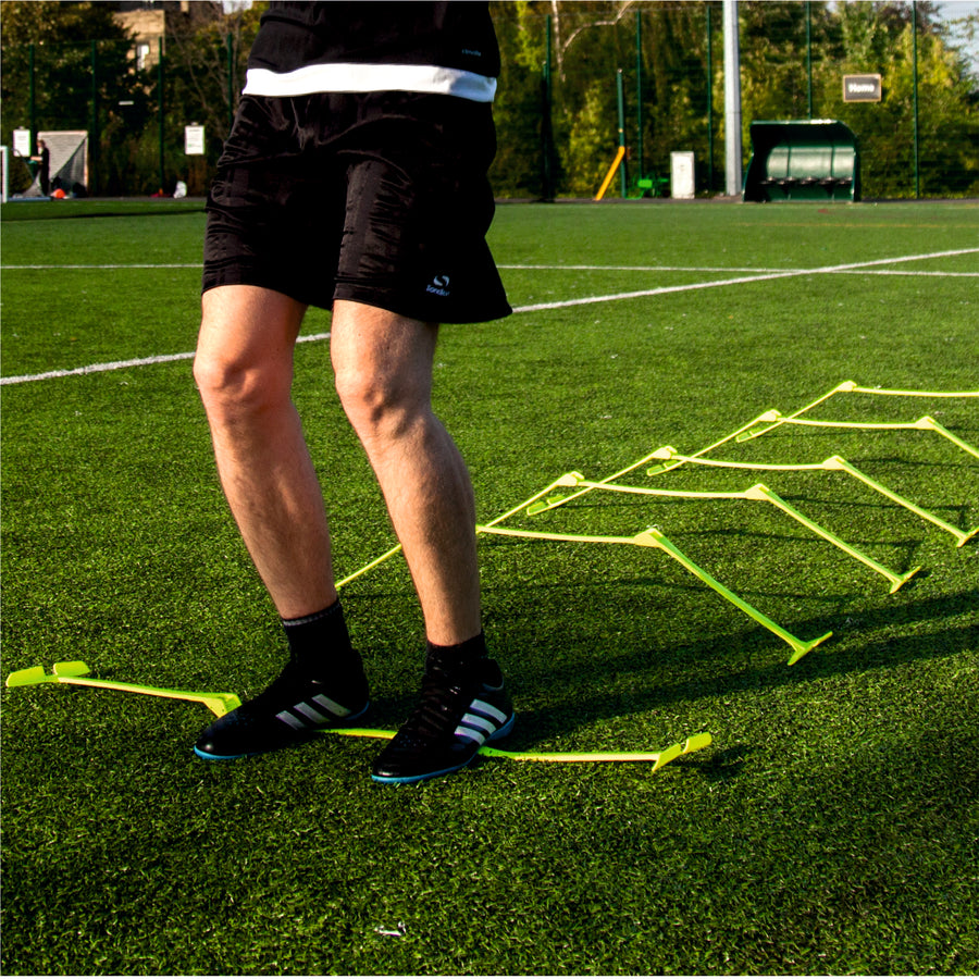 Jugador pasando entre vallas de entrenamiento regulables amarillas bajas en un campo de césped artificial.
