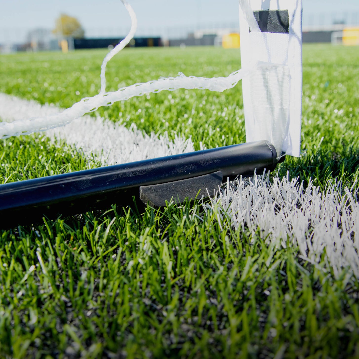 Detalle de la KICKSTER Elite 370 x 180 cm: un tubo negro de la base sobre una línea blanca del campo junto a la funda blanca del poste.