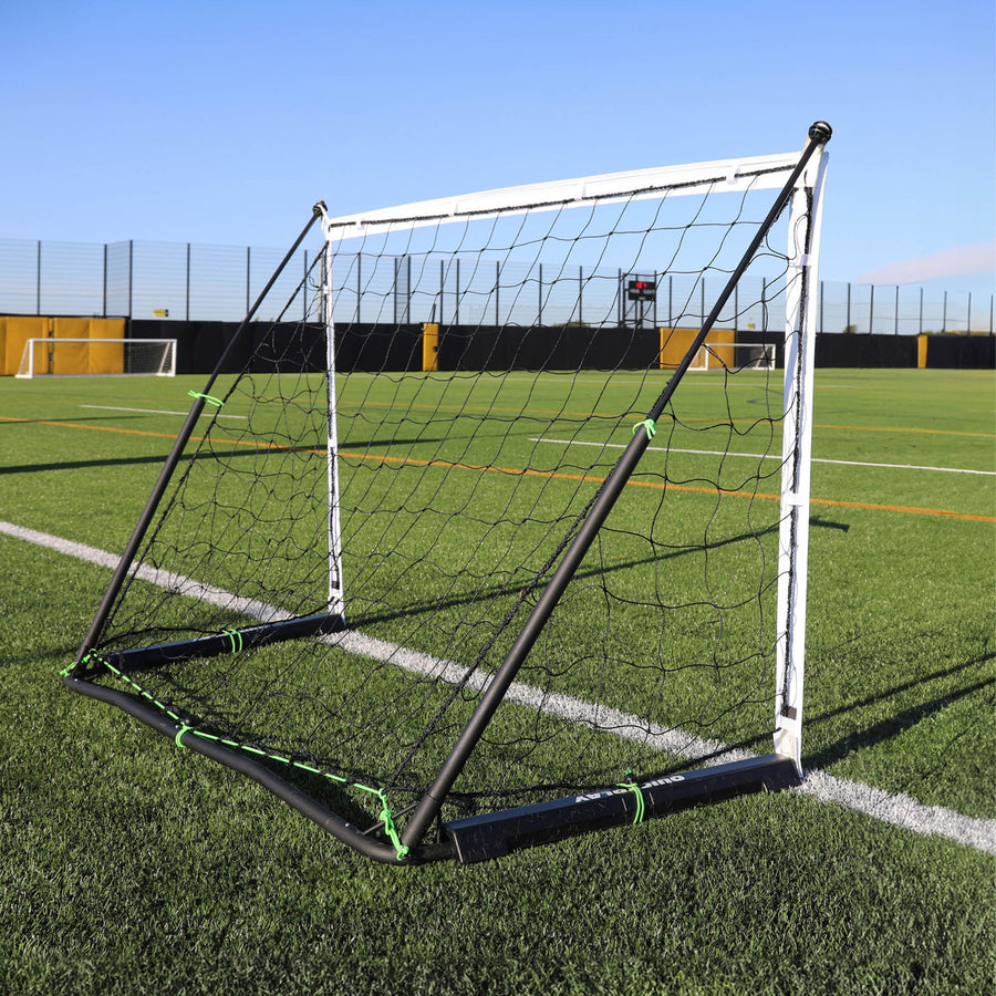 KICKSTER Elite 150 x 100 cm vista desde una esquina trasera en un campo de césped artificial, con el marco negro y las bridas verdes.