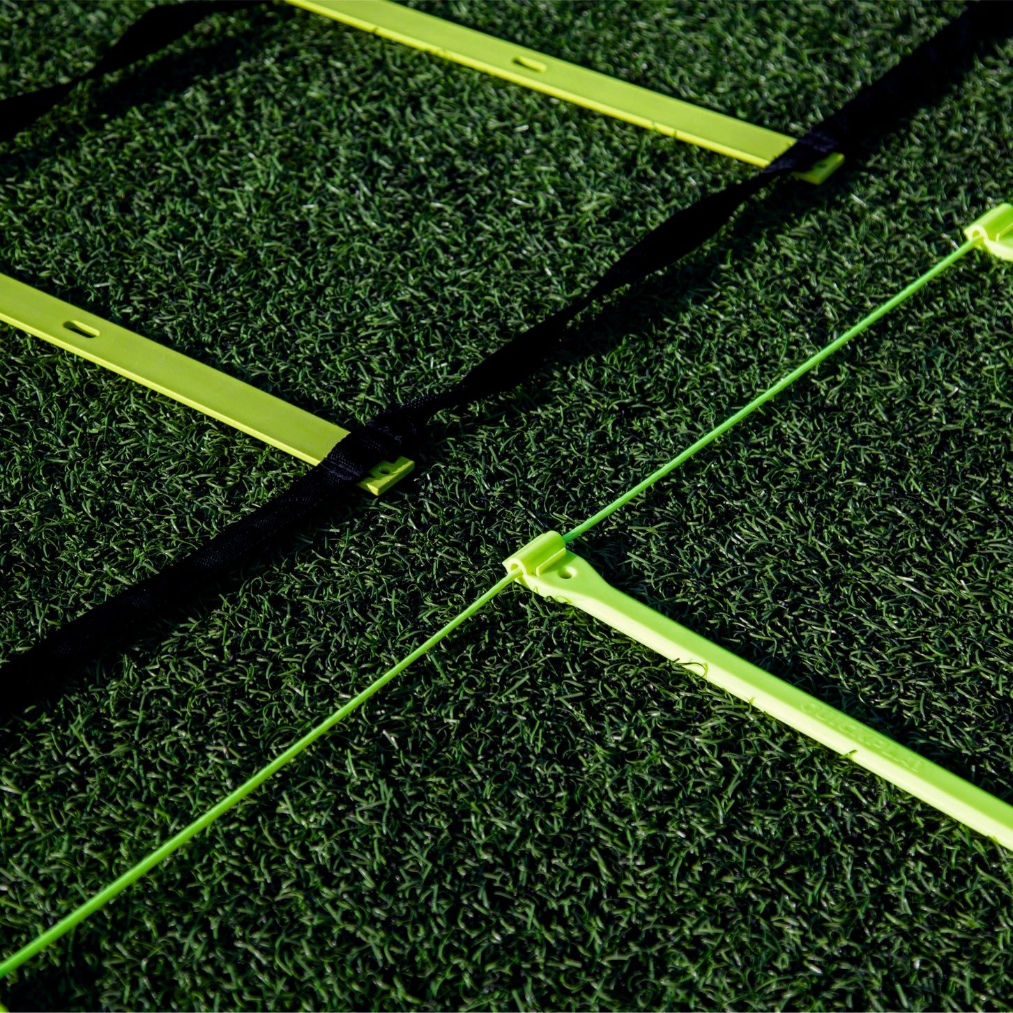 Primer plano de peldaños amarillos de la escalera de agilidad sobre césped artificial, una escalera con correas negras y otra con un fino cordón verde.