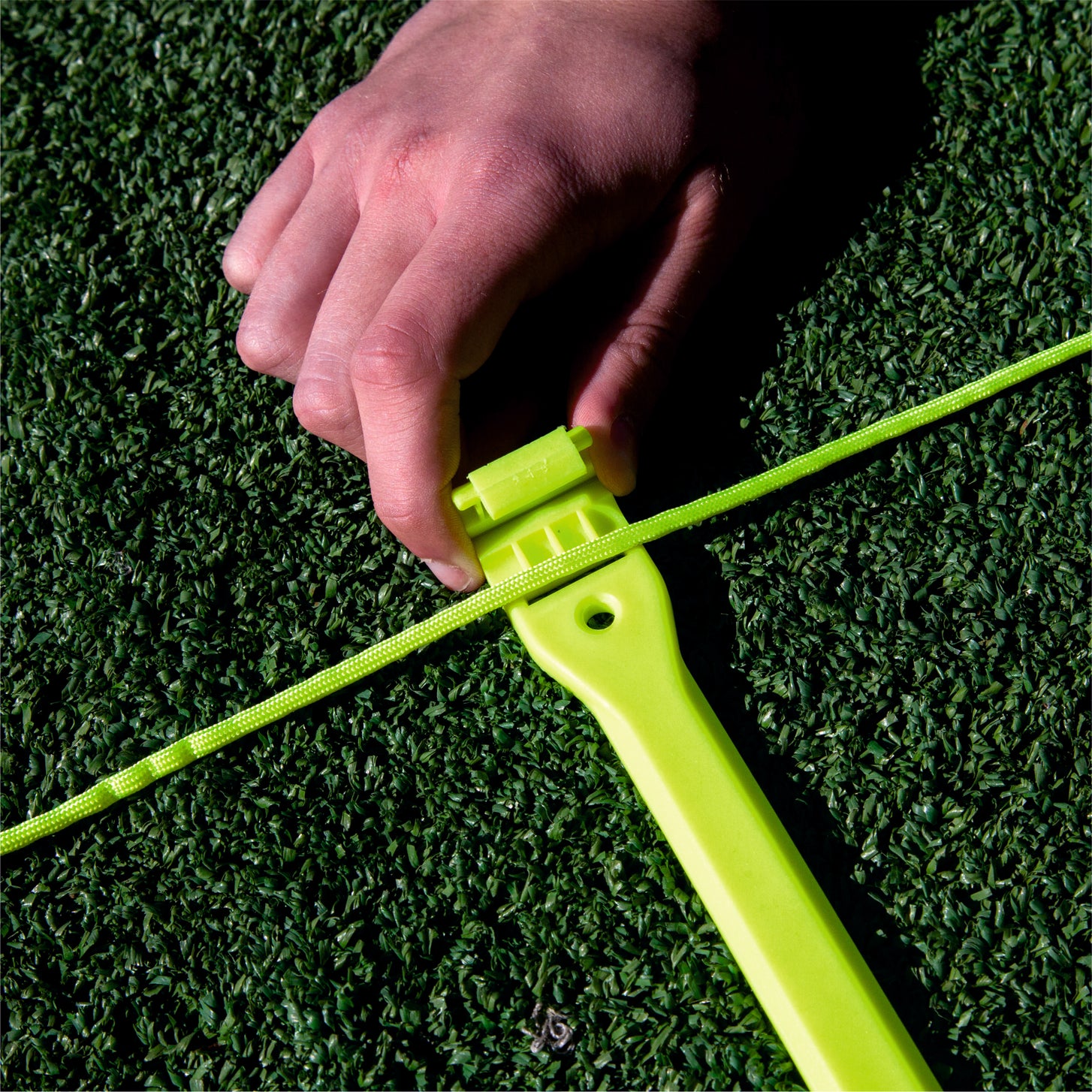 Primer plano de una mano enganchando el cordón de la escalera de agilidad en un peldaño amarillo sobre césped artificial.