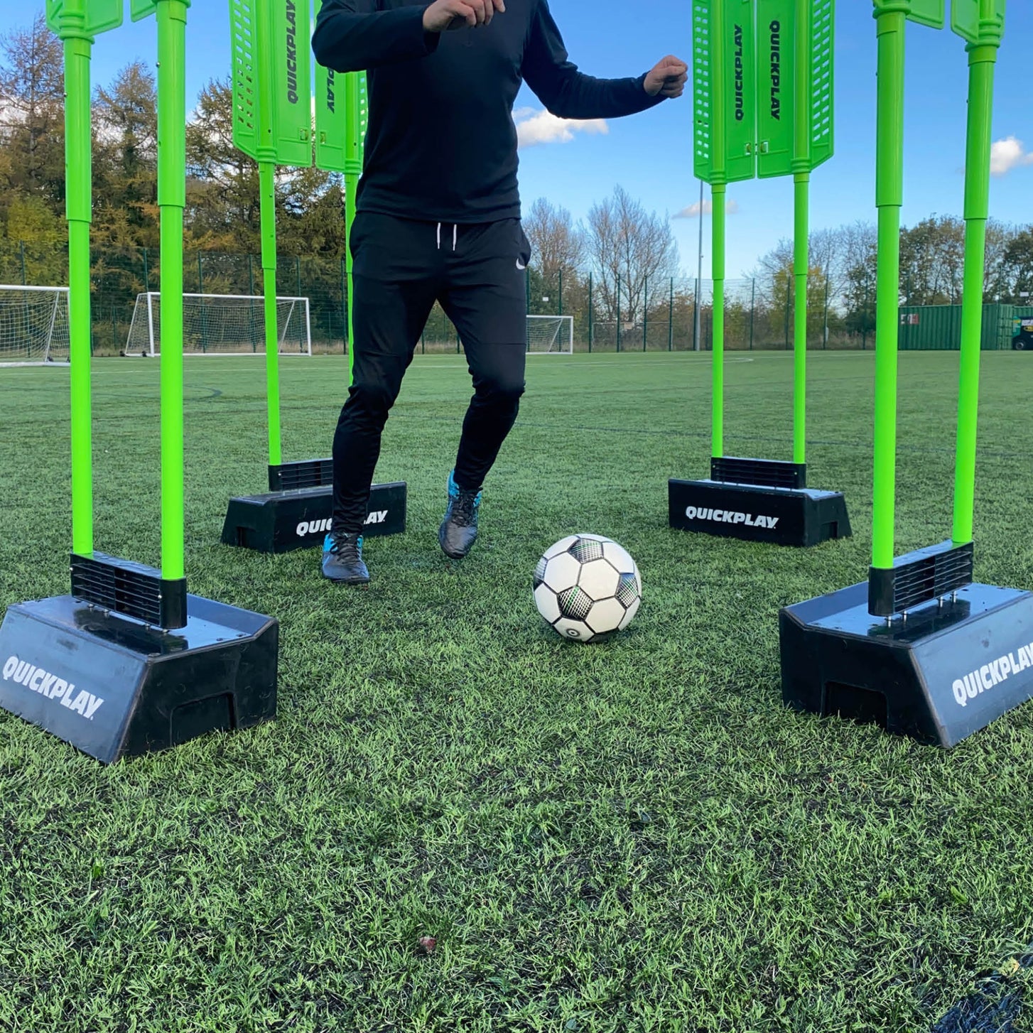 Tablas de rebote de doble ángulo REPLAY Block sosteniendo cuatro maniquíes verdes, con un jugador moviendo el balón entre ellos sobre césped artificial.