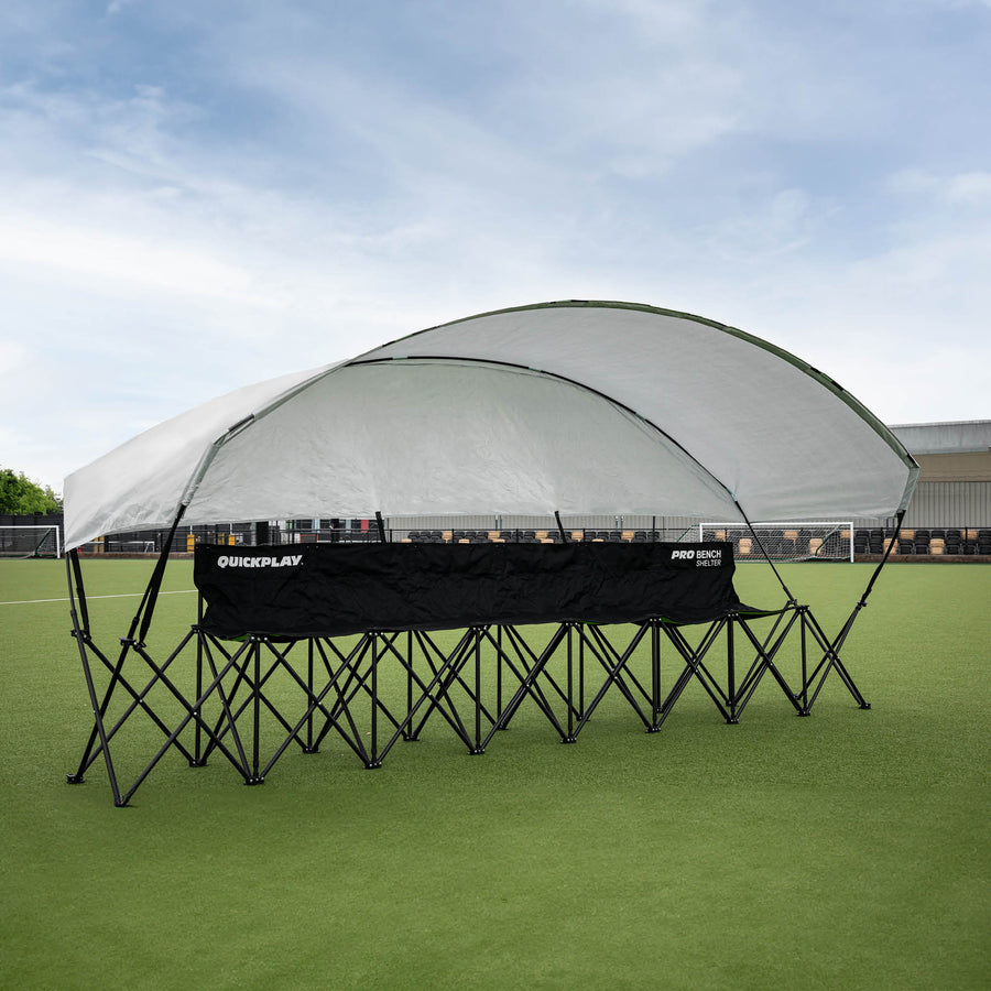 Banquillo de suplentes cubierto PRO Bench Shelter de 6 plazas con su toldo gris, montado en un campo de césped artificial.