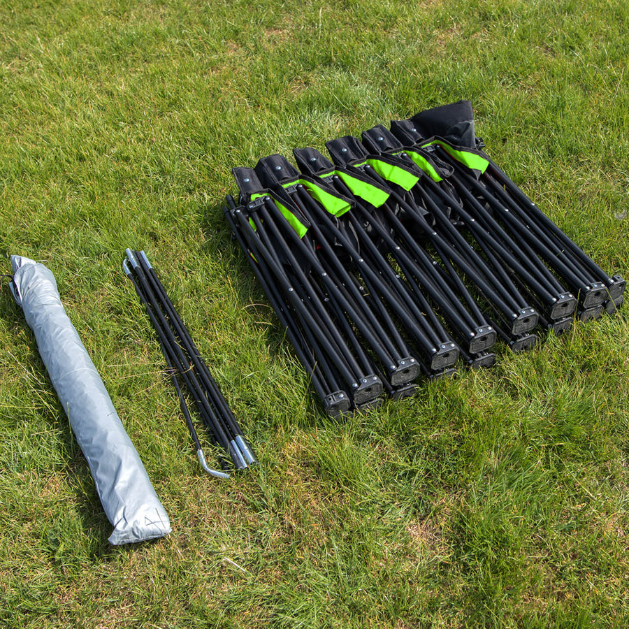 Piezas del PRO Bench Shelter dispuestas sobre la hierba: el marco del banquillo plegado, las barras del toldo y el toldo gris enrollado.