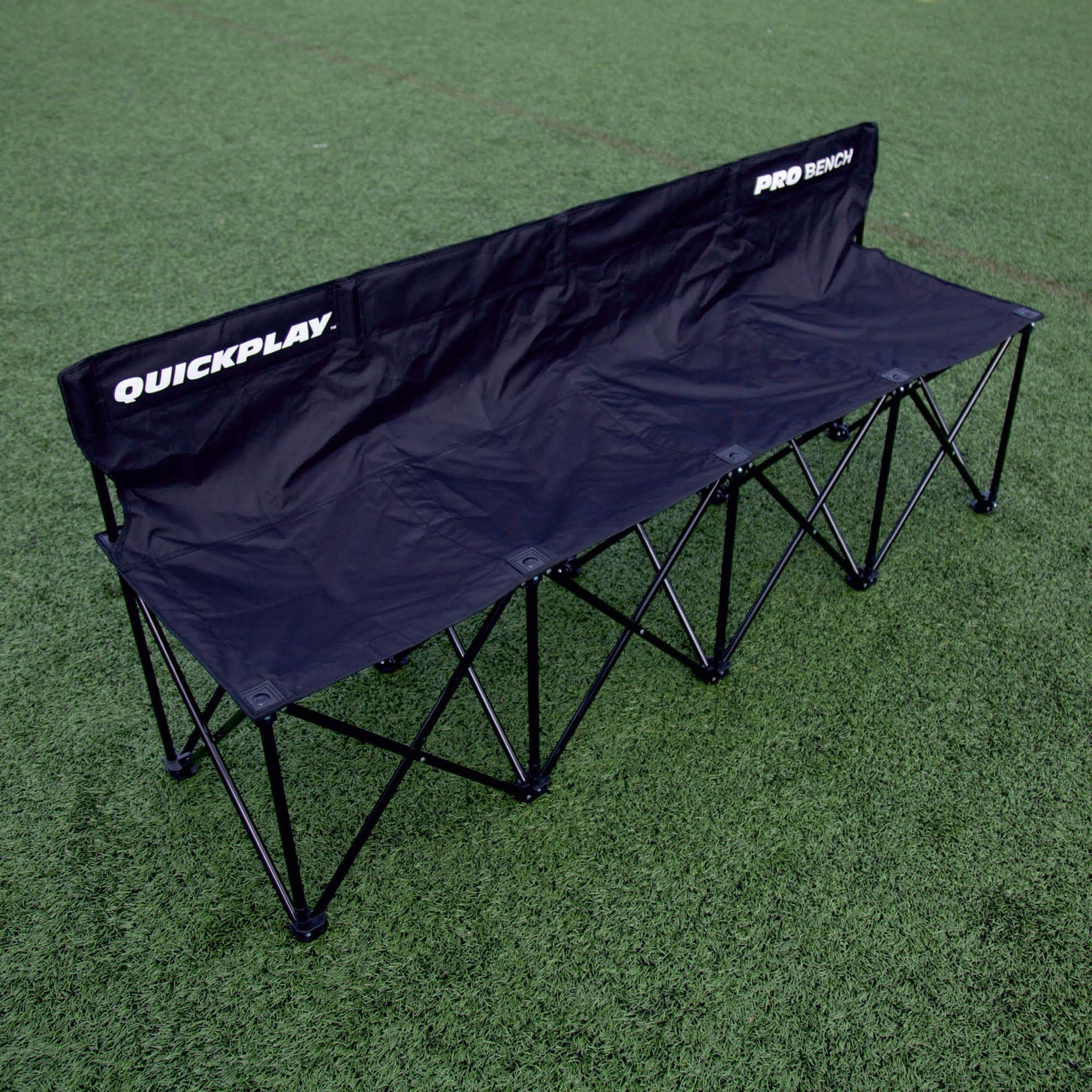 Banquillo de suplentes PRO Bench de 4 plazas, negro, desde un ángulo elevado sobre césped artificial, con QUICKPLAY y PRO BENCH en el respaldo.