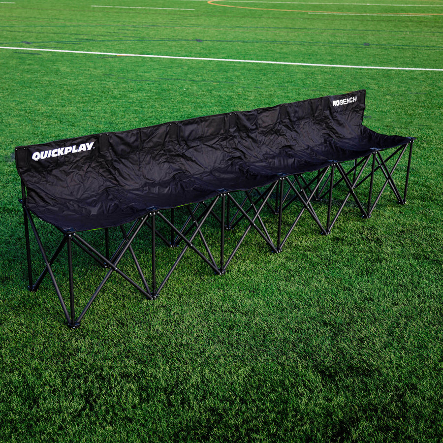 Banquillo de suplentes PRO Bench de 6 plazas, negro, desplegado en un campo de césped artificial, visto desde la esquina delantera.