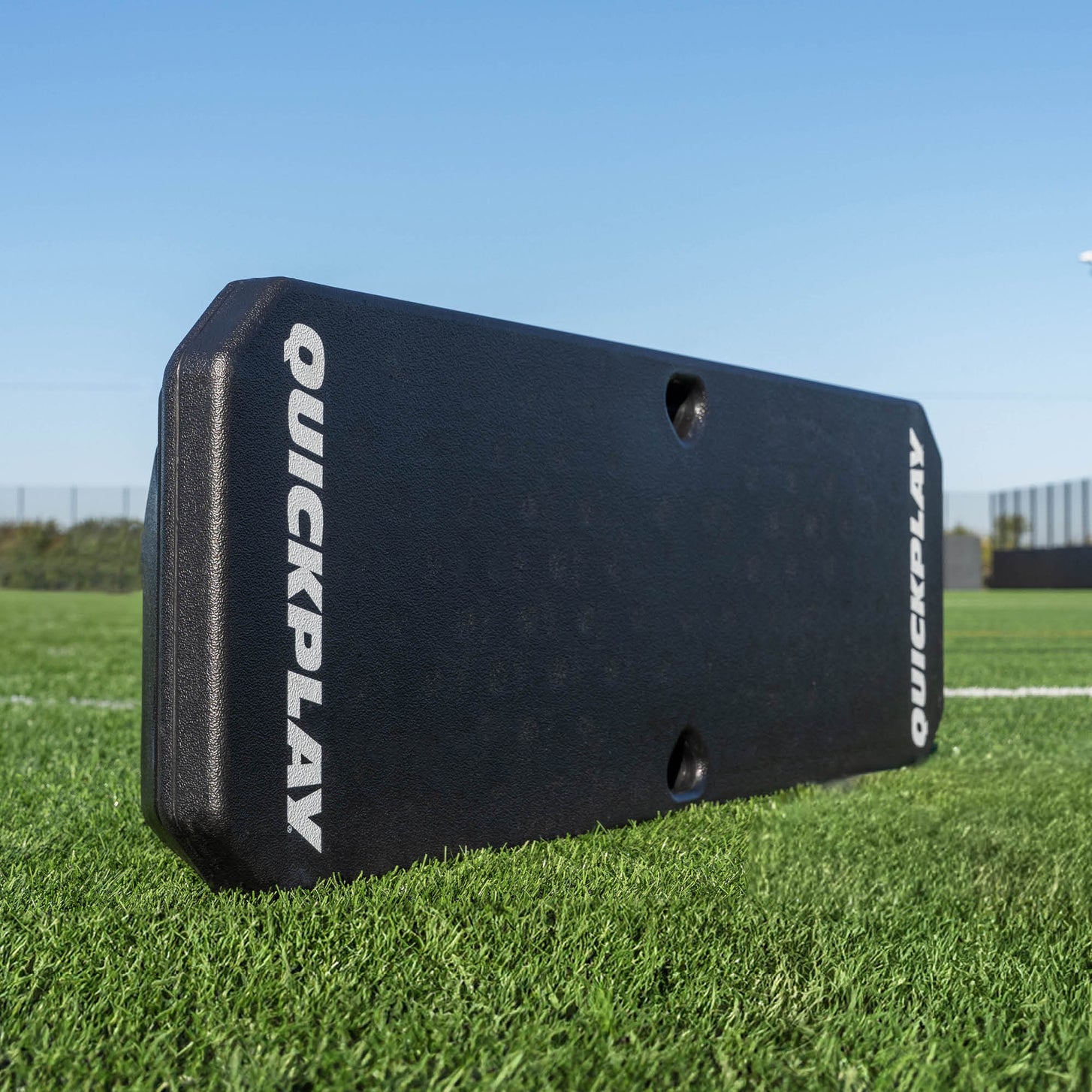 Tabla de rebote de fútbol REPLAY Boombox, negra con logotipos blancos QUICKPLAY, de pie sobre césped artificial.