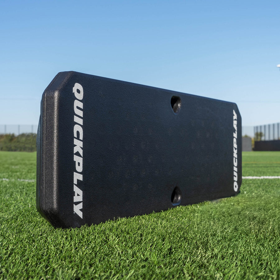 Tabla de rebote de fútbol REPLAY Boombox, negra con logotipos blancos QUICKPLAY, de pie sobre césped artificial.