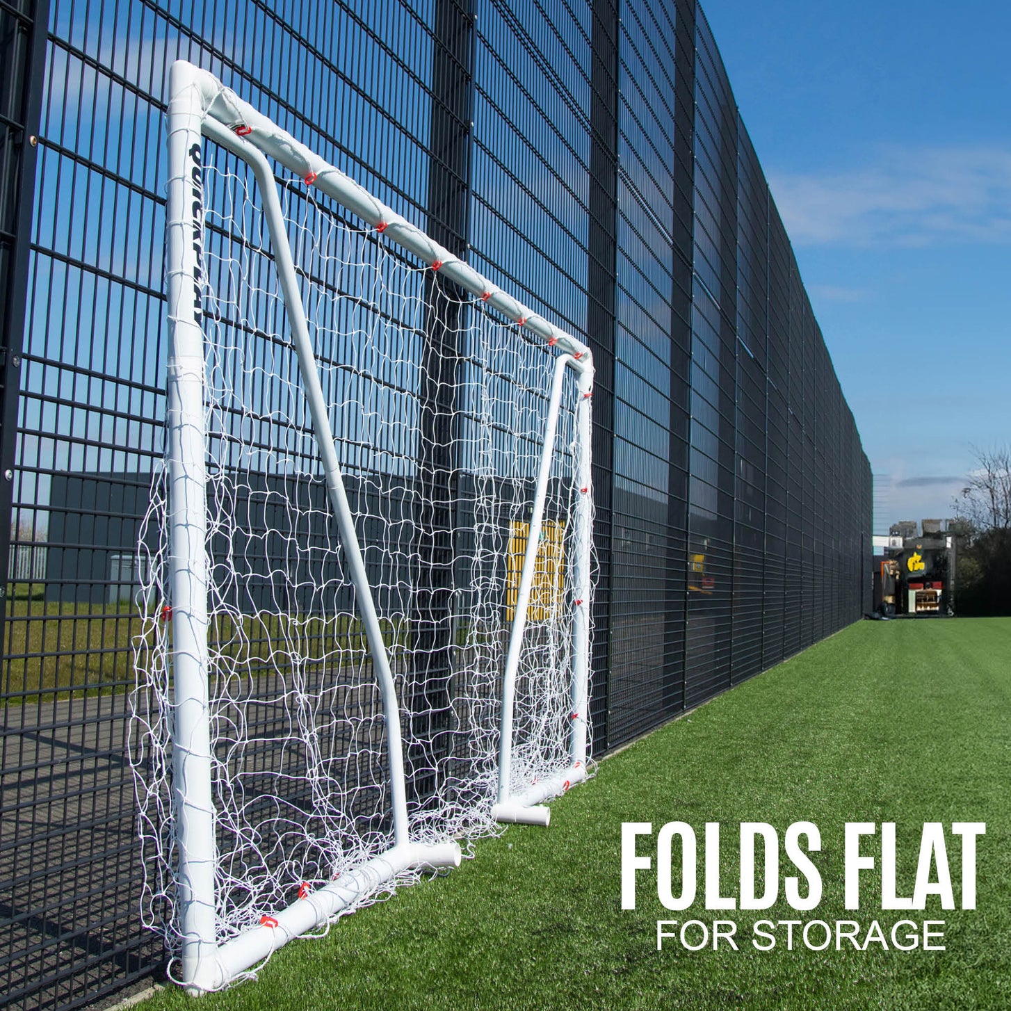 Q-FOLD Match 300 x 200 cm plegada en plano contra una valla en un campo de césped artificial, con el texto "Folds flat for storage".