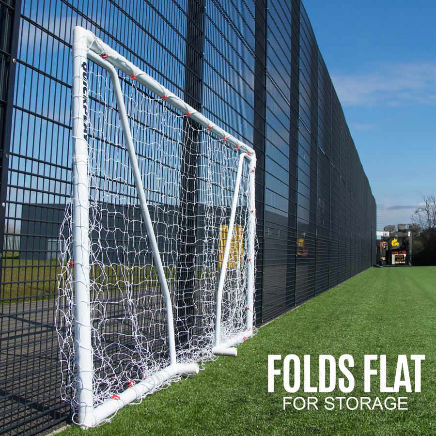 Q-FOLD Match 300 x 200 cm plegada en plano contra una valla en un campo de césped artificial, con el texto "Folds flat for storage".