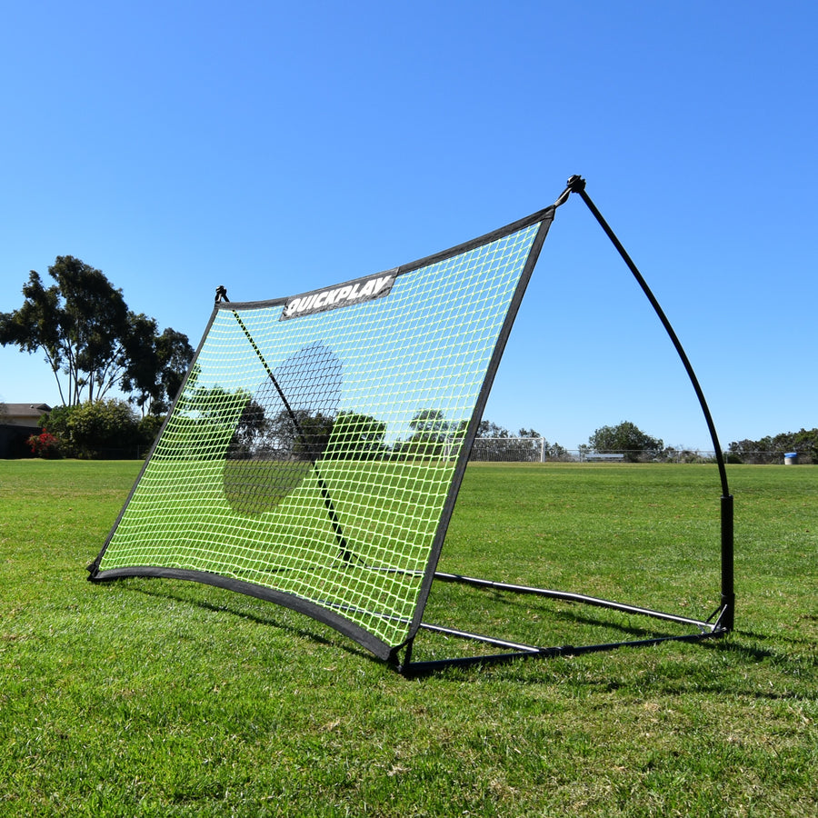 Rebotador de fútbol TEKKERS Net 150 x 100 cm sobre hierba al sol, visto desde una esquina delantera, con su red verde.