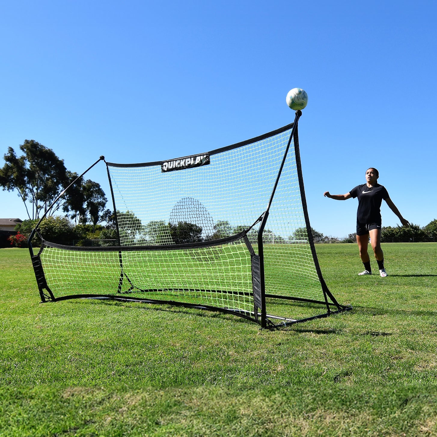Jugador esperando un balón que rebota hacia arriba en el rebotador de fútbol TEKKERS Trainer con doble red en un campo de hierba.