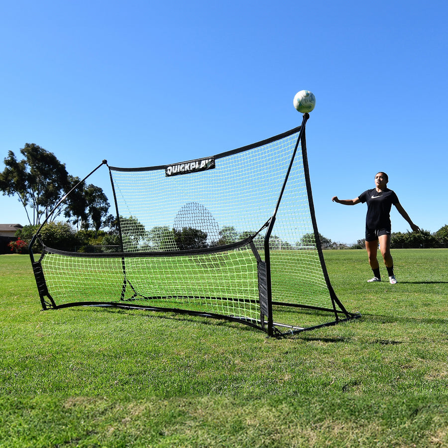Jugador esperando un balón que rebota hacia arriba en el rebotador de fútbol TEKKERS Trainer con doble red en un campo de hierba.